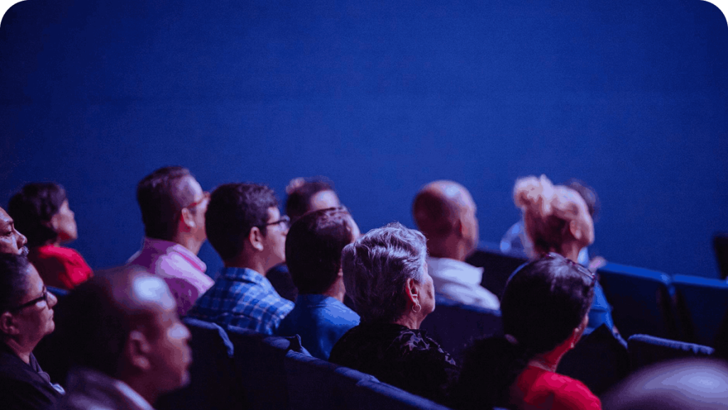 Audience members sitting in a dimly lit theater.